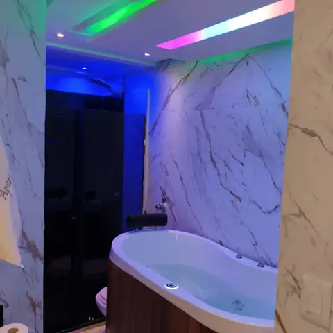 Banheira de hidromassagem com parede de mármore e iluminação colorida no forro