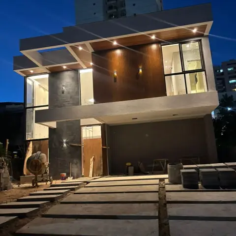 Casa duplex à noite, com fachada em madeira e pedra, luzes embutidas e jardim
