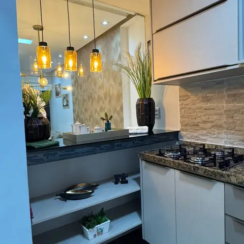 Cozinha com bancada de granito escuro, revestimento bege na parede e três luminárias pendentes cor de âmbar