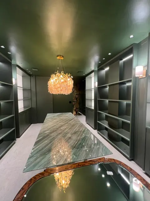 Ambiente verde com estantes iluminadas, lustre e bancada de pedra