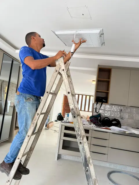 Eletricista instalando luminária no forro de gesso de uma cozinha