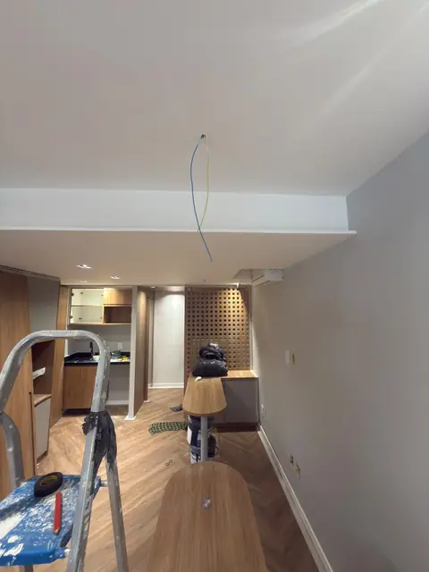 Sala em obra com forro de gesso pronto, marcenaria instalada e fios do lustre