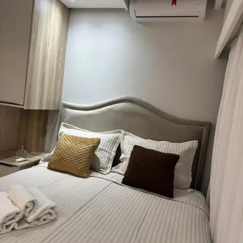 Quarto com cabeceira estofada, cama de casal arrumada com almofadas e criado-mudo branco