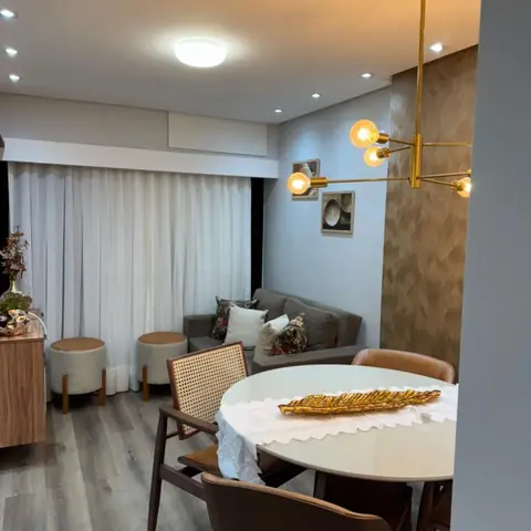 Sala de jantar com lustre dourado, mesa redonda, cadeiras de palhinha e sofá cinza ao fundo